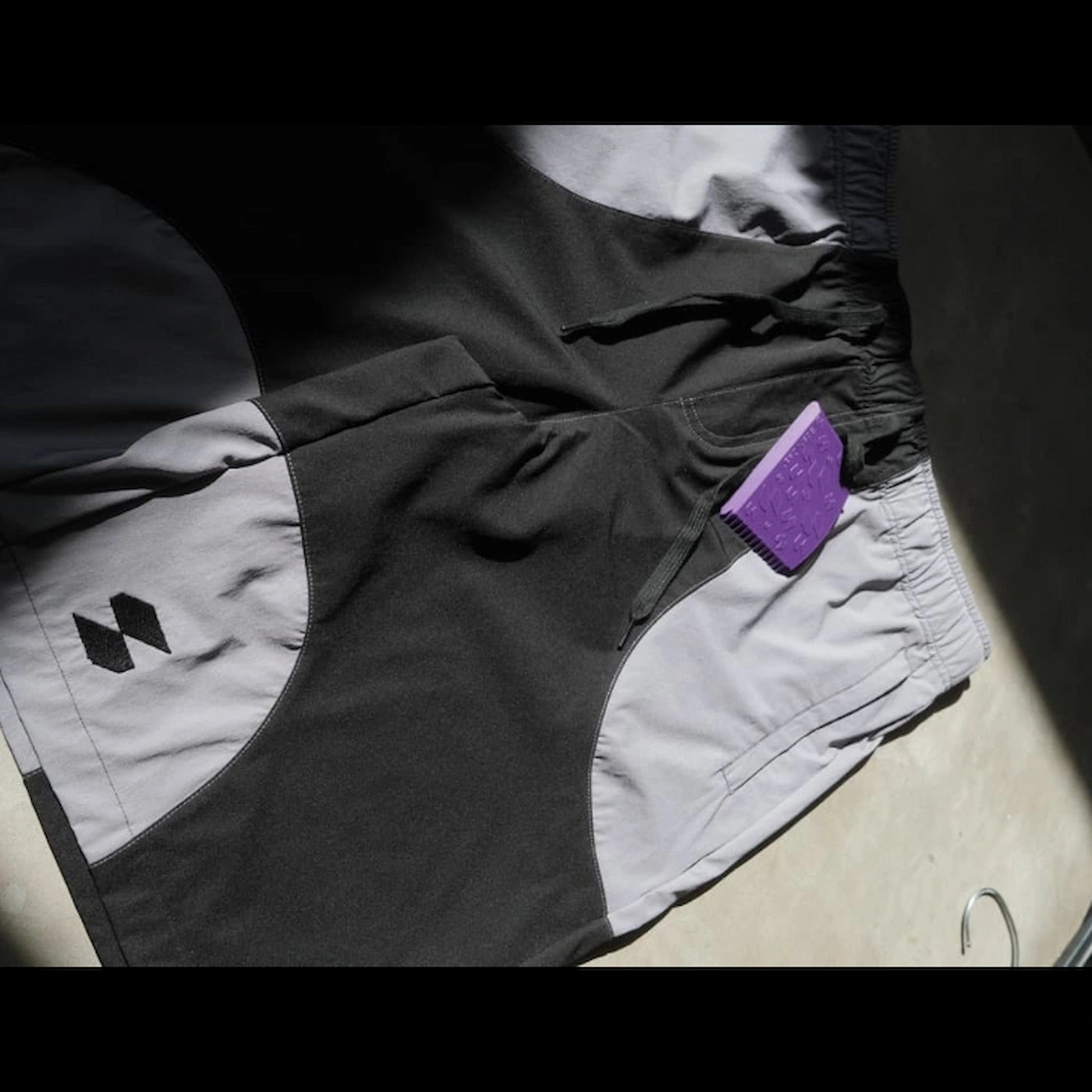 Close-up of black and gray Scerfer Baggy Boardshorts with elastic waistband and included surf wax comb accessory.