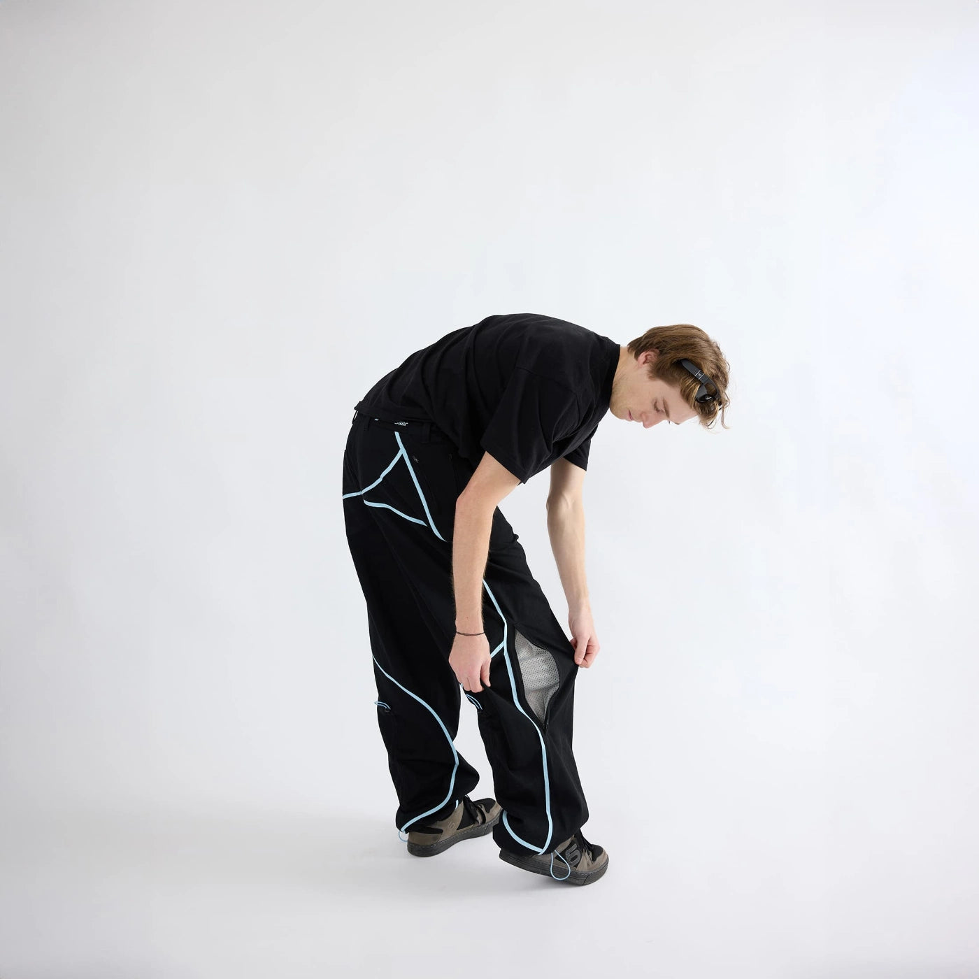 Model adjusting zipper leg vent on black Curvy Baggy Pants featuring curved seam design and built-in belt for active streetwear.